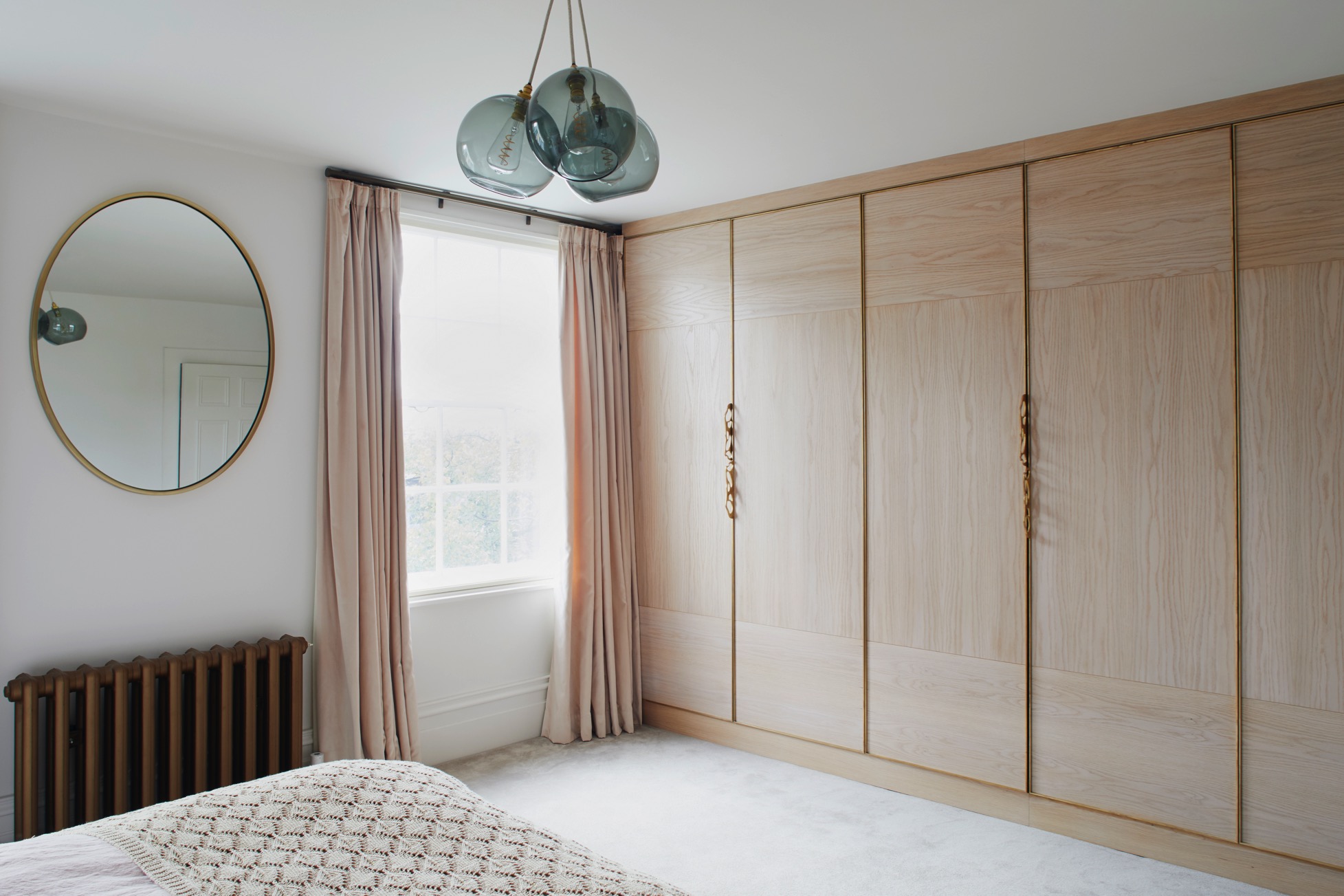 Bespoke bedroom cabinetry in soft pink with brass handles and details