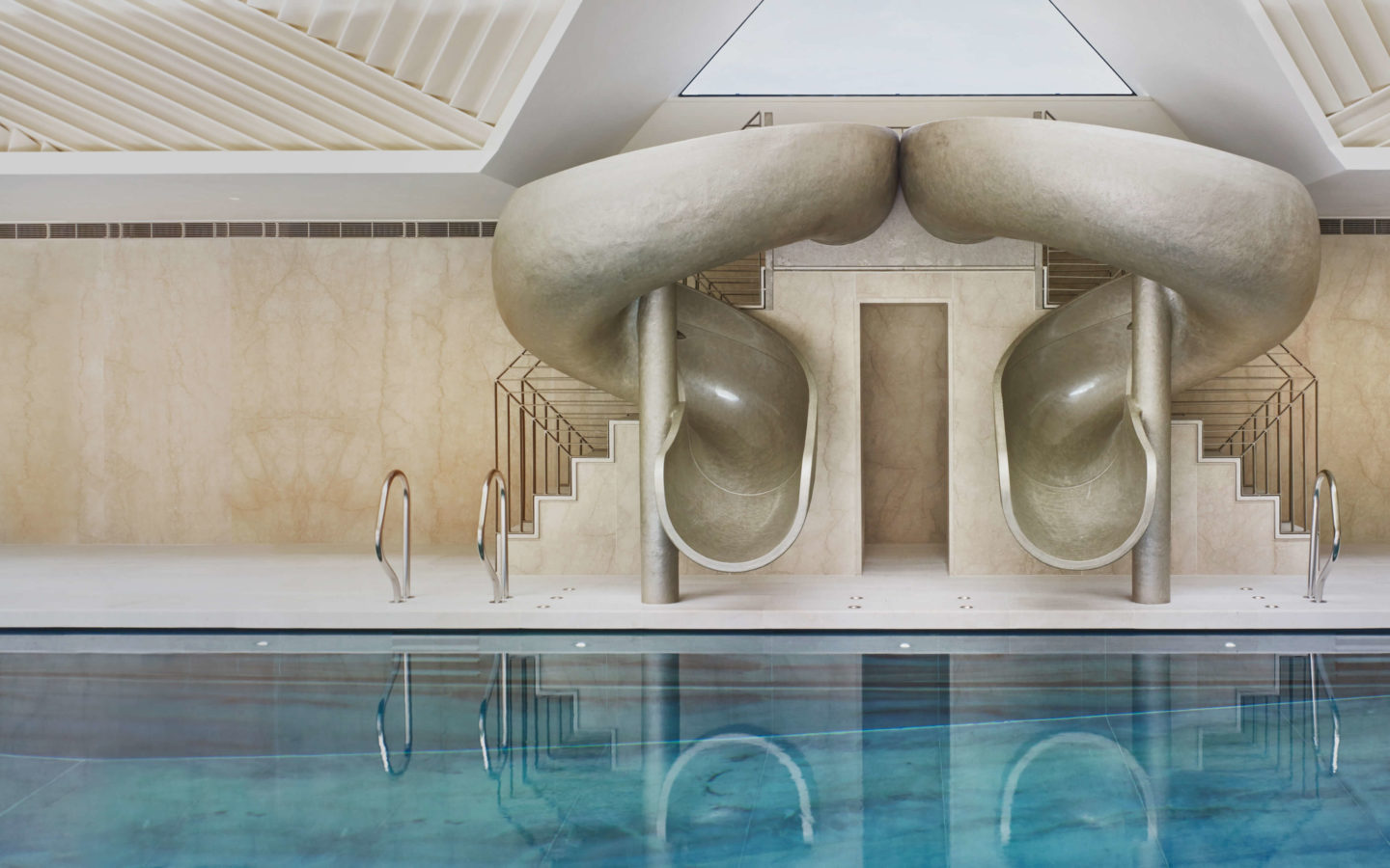 Spectacular double-helix pool slide in gold resin beside an indoor pool.