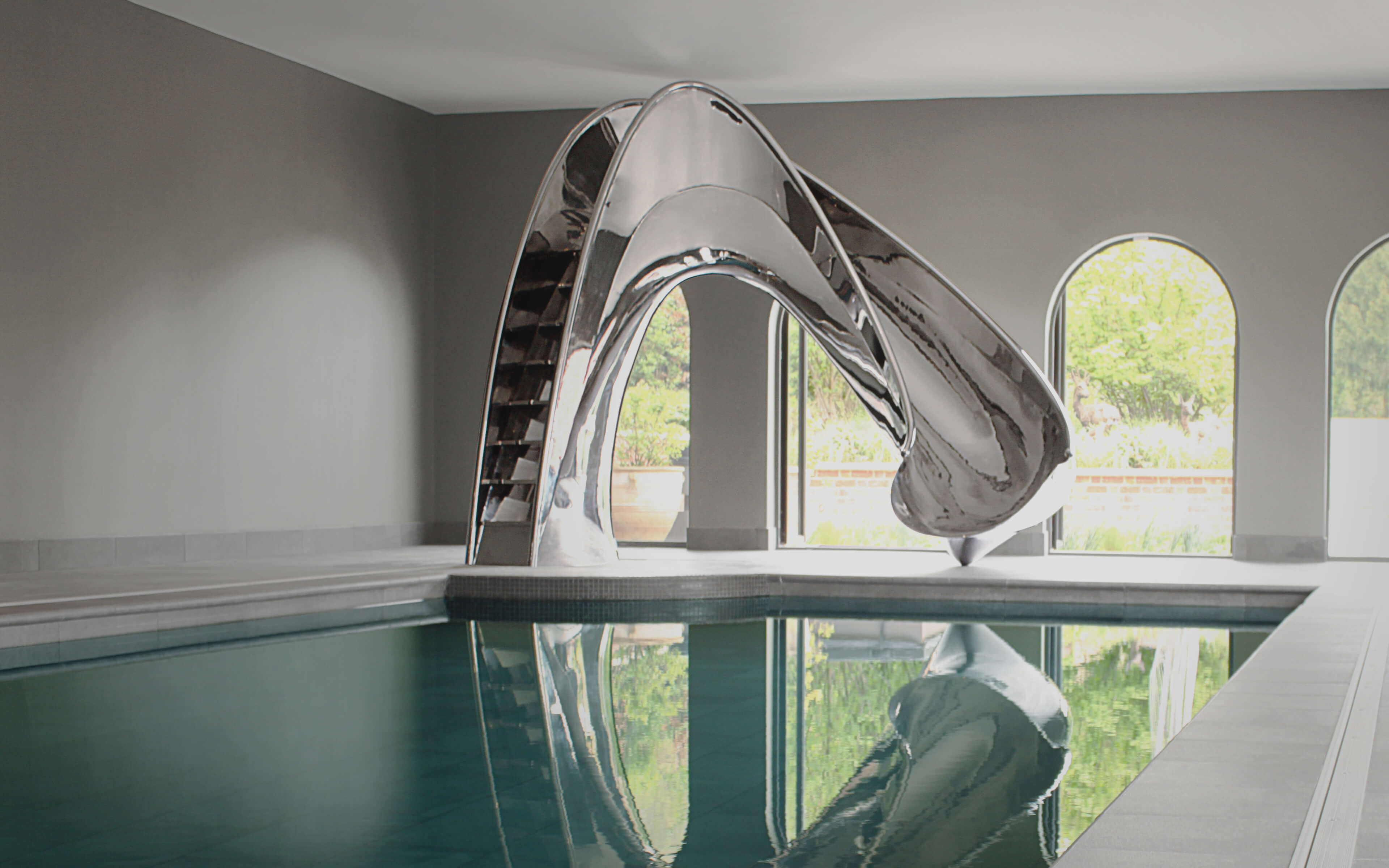 Mirror polished stainless steel pool slide in architectural pool pavilion.