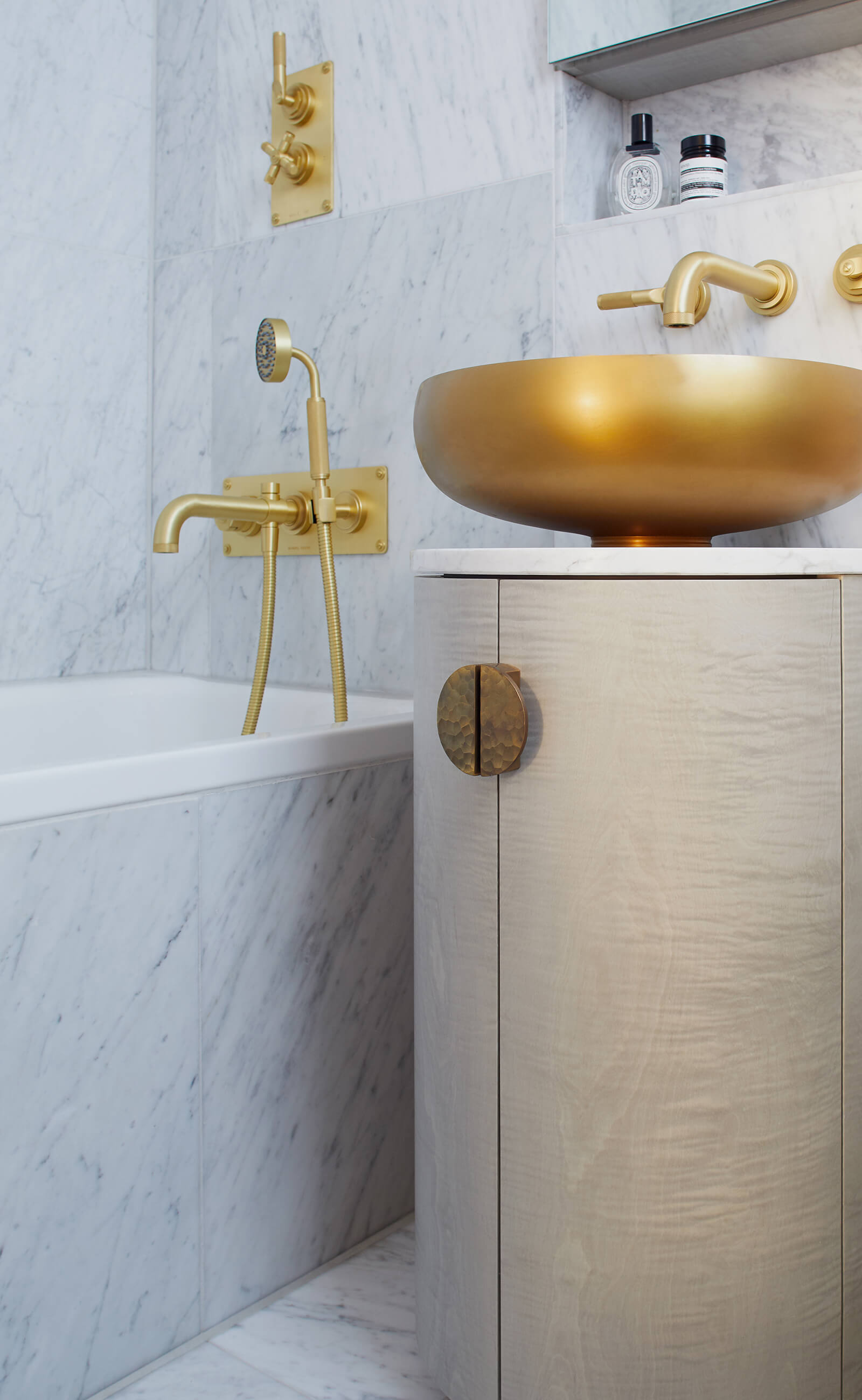 Grey bathroom vanity cabinet with brass sink and fittings in a bathroom lined with carrara marble