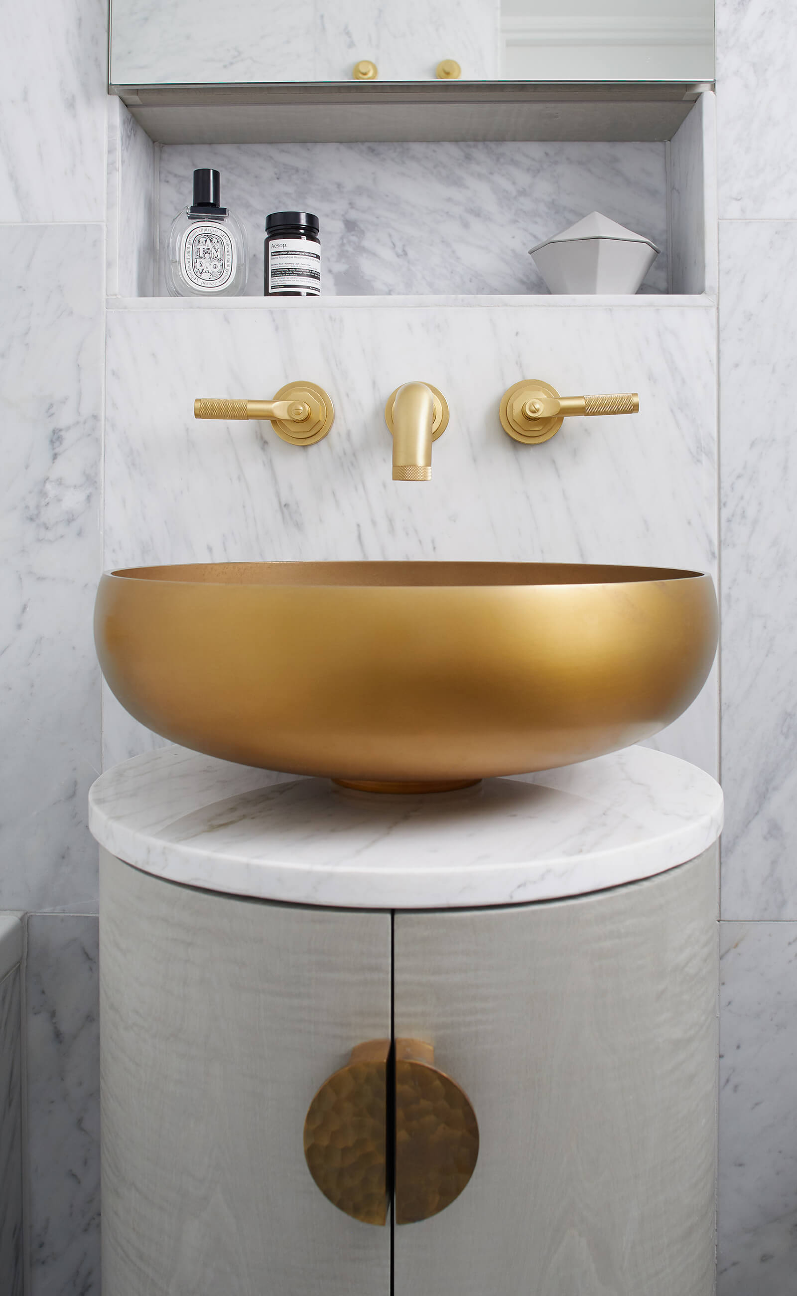 Round brass basin on grey bathroom cabinet with carrara marble walls