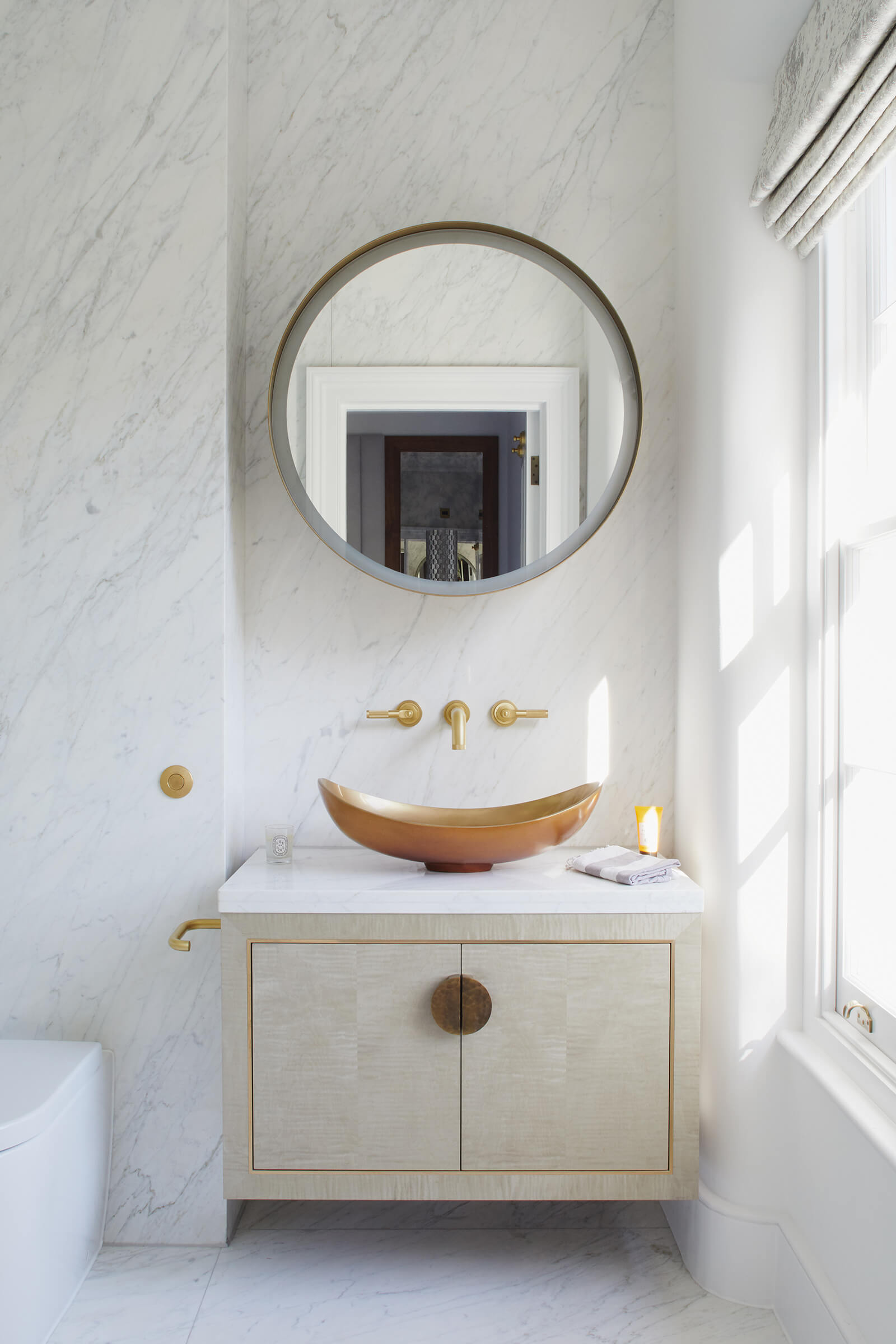 bathroom vanity cabinet with brass details below a brass sink in a carrara marble bathroom