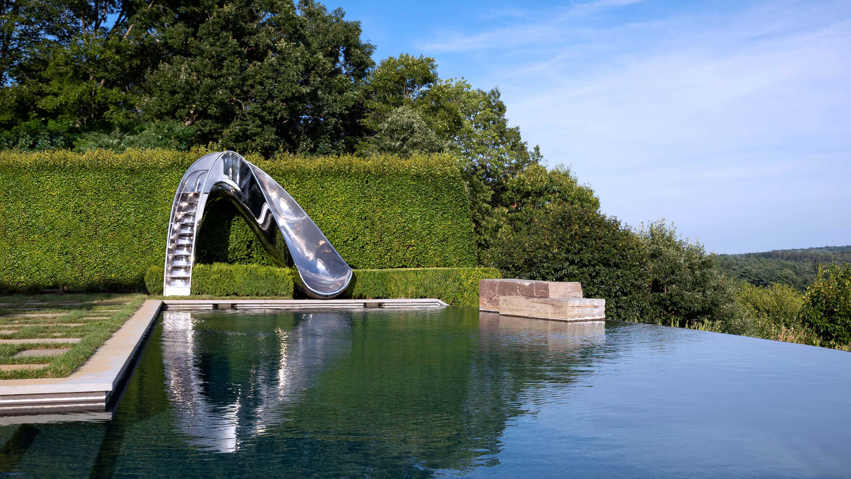 Luxury stainless steel swimming pool slides. Captured across pool with view over the Hamptons.
