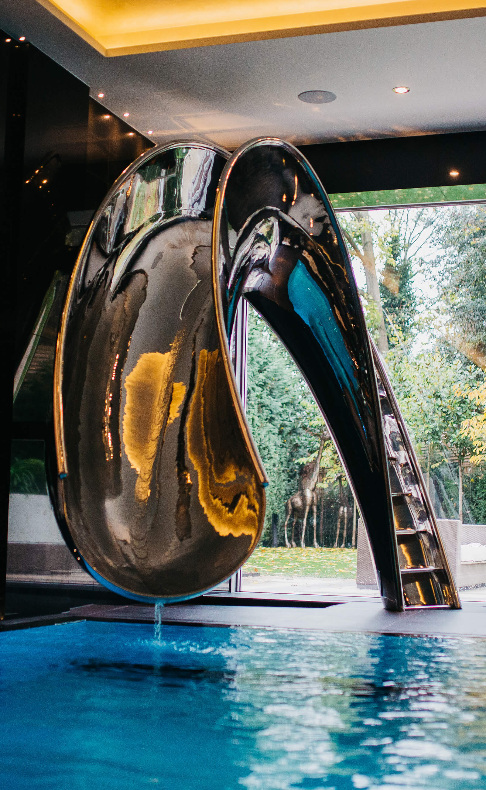 Reflex luxury swimming pool slides are custom made in polished metal. Reflecting pool side lighting as an indoor swimming pool slide.