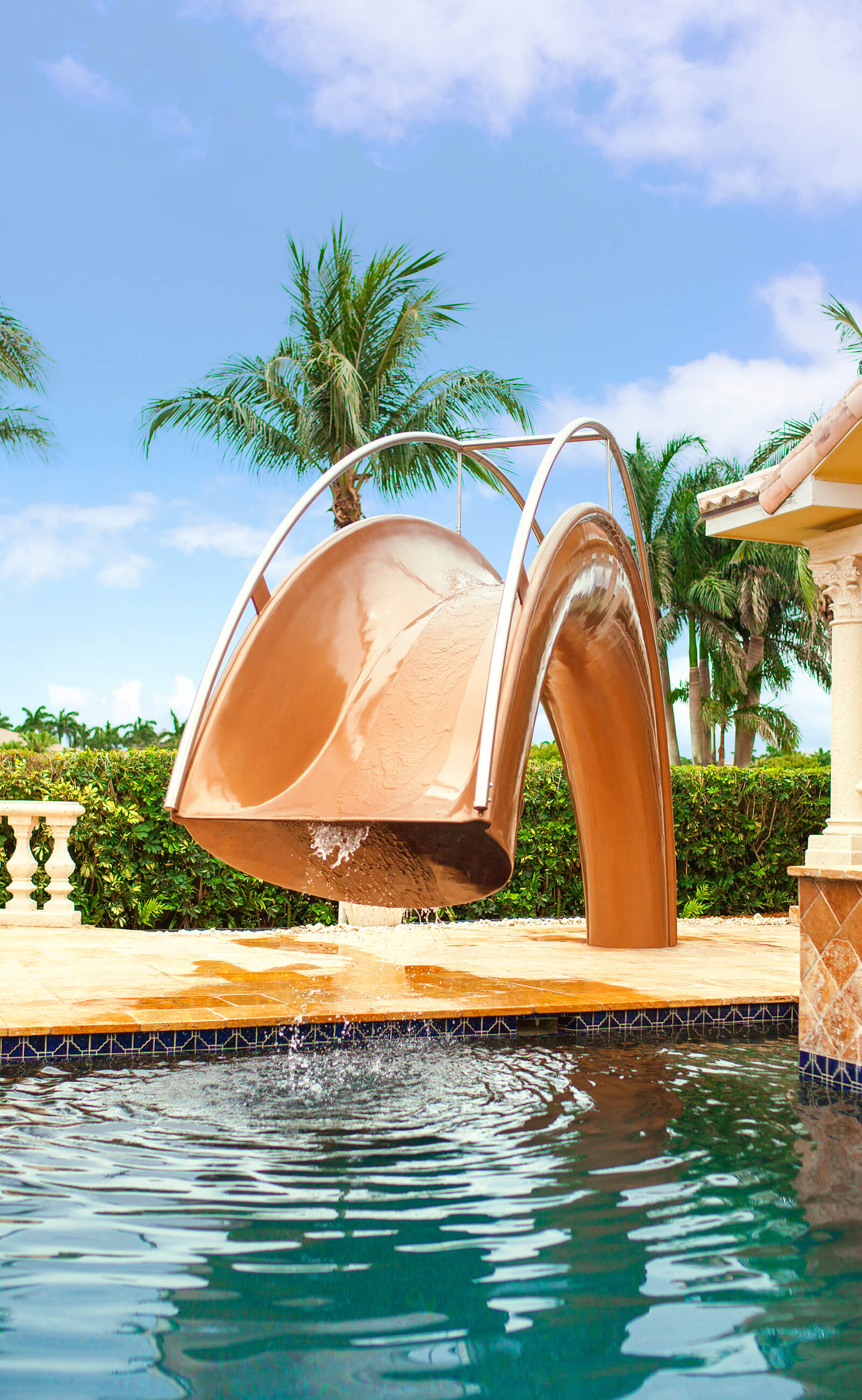 Water cooling system designed into family pool slide next to outdoor pool and palm trees.
