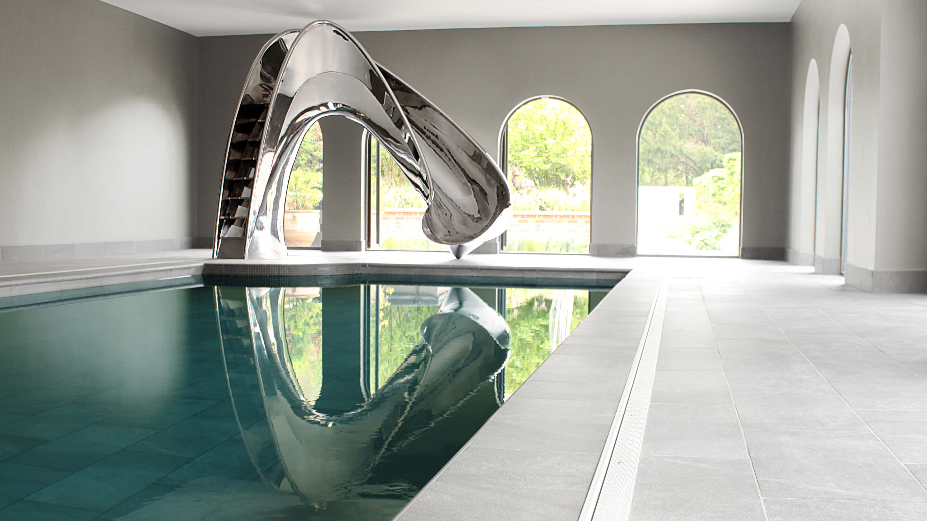 View of stainless steel pool slide across indoor pool with 3 arch windows behind