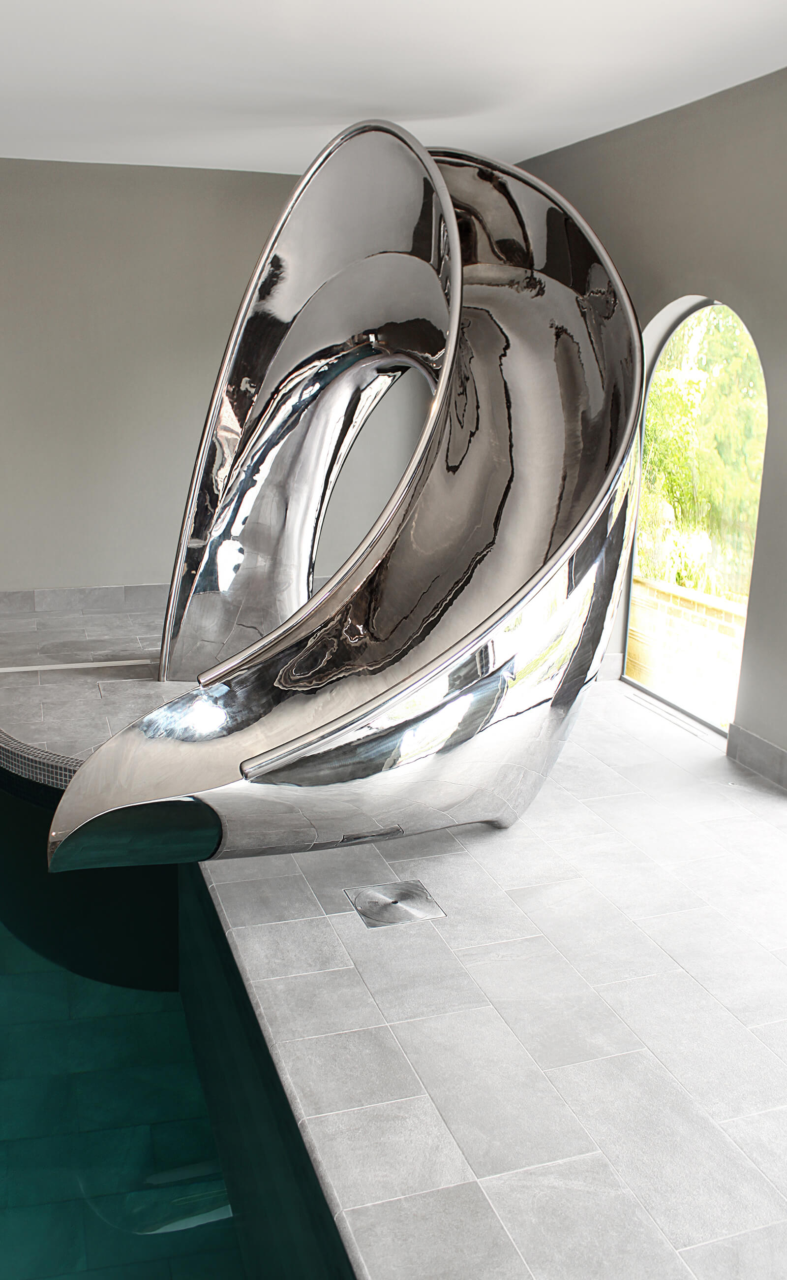 Sculptural twist of the slide curving towards the water of the indoor pool.