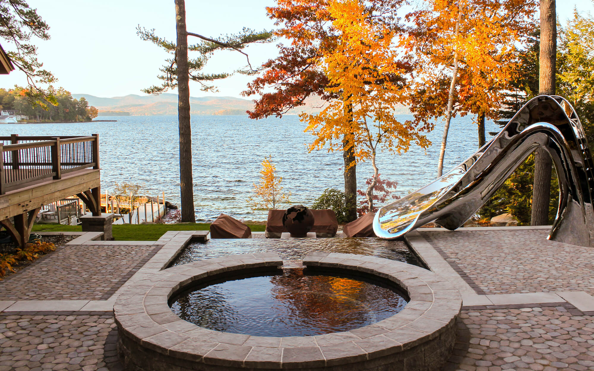 Shinny metal pool slide besides a lake in fall, designed in collaboration with water shape designers