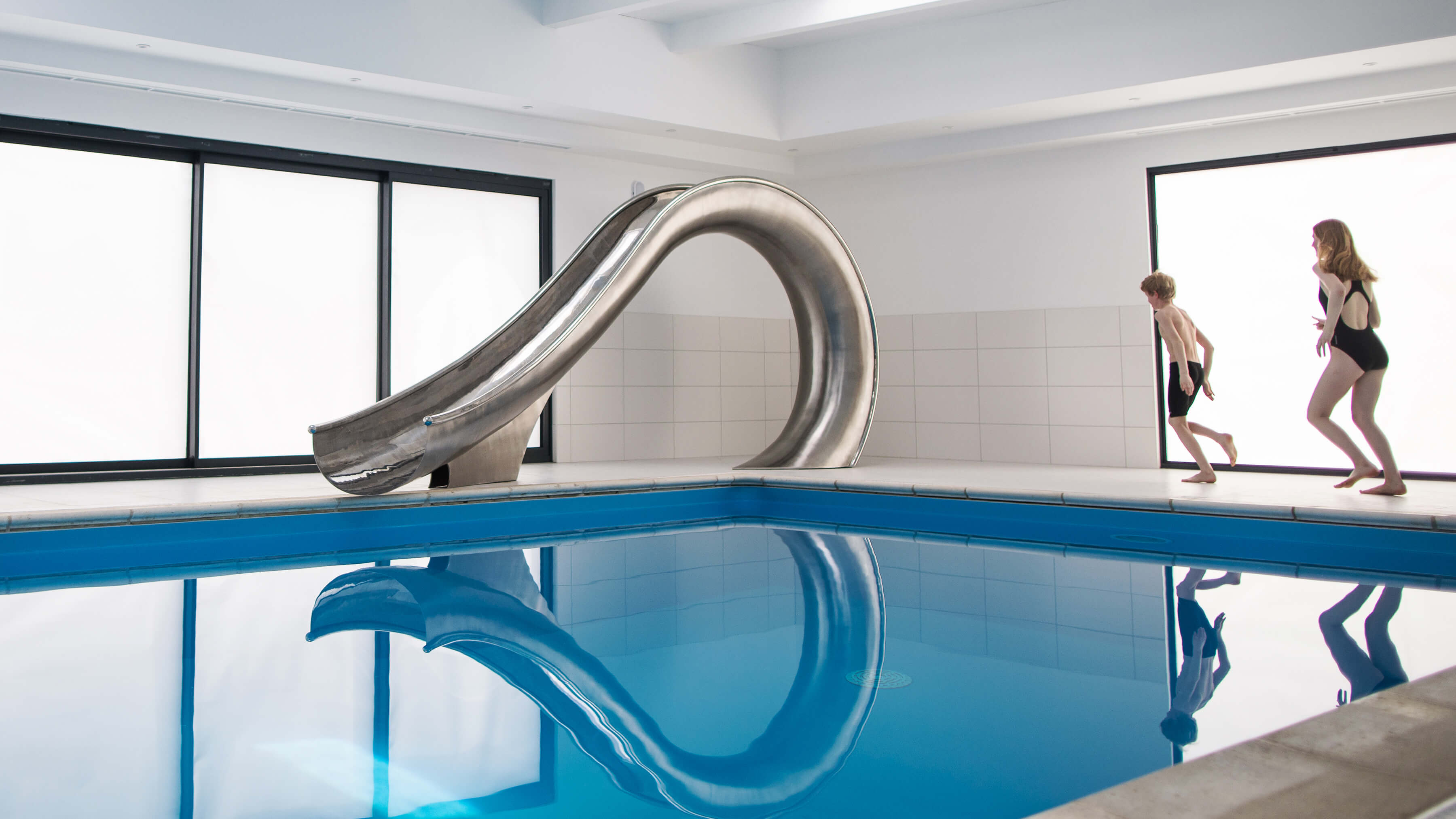 Two children excitedly running towards their new indoor swimming pool slide.