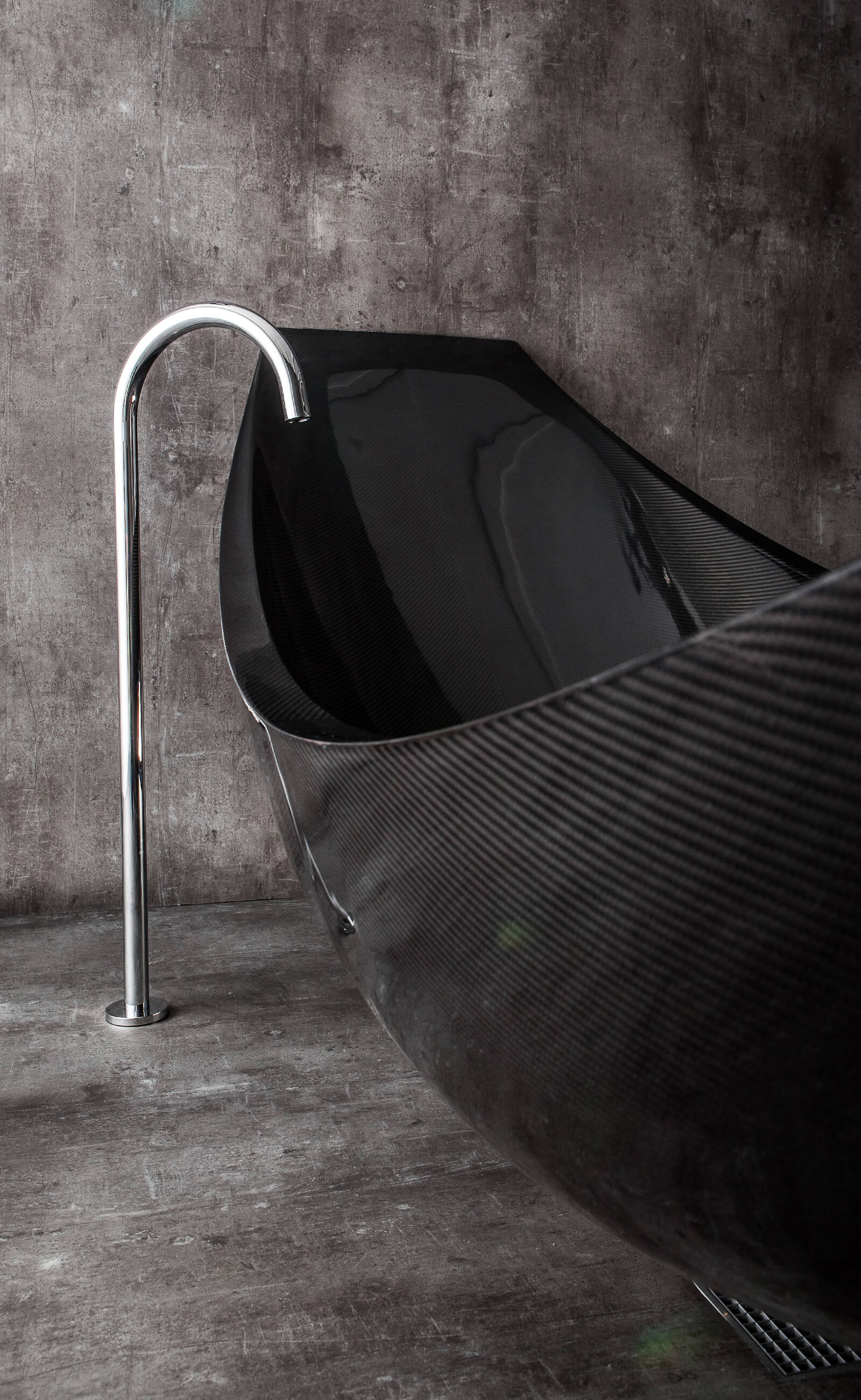 Detail of floor standing bath tap next to black suspended bath in polished concrete wet room manufactured by Splinterworks