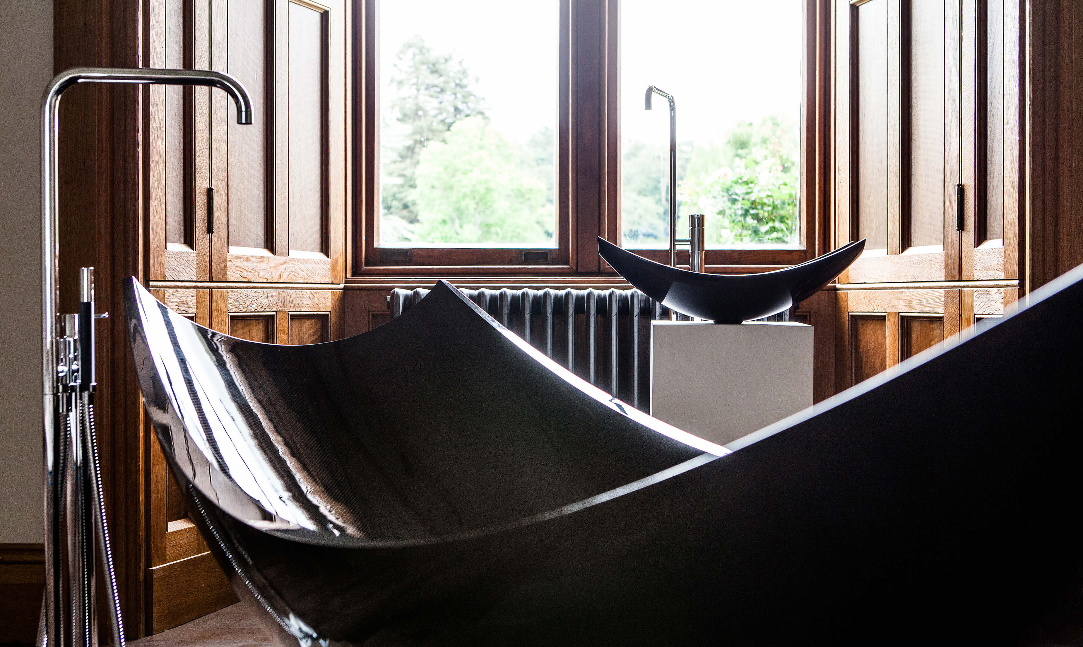 Close up of black freestanding hammock bath and basin next to window.