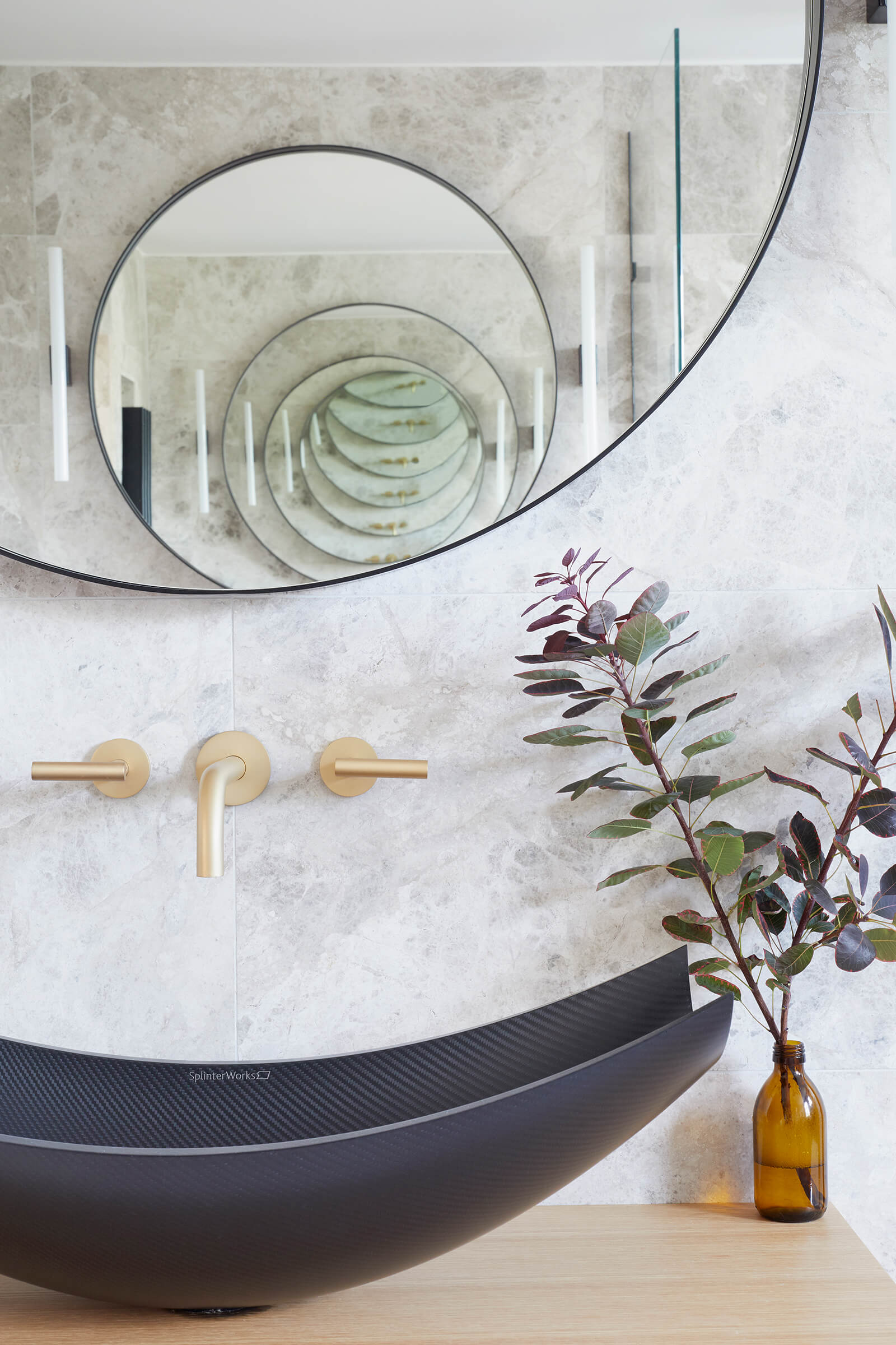 Black vanity basin below gold forcet and round mirror.