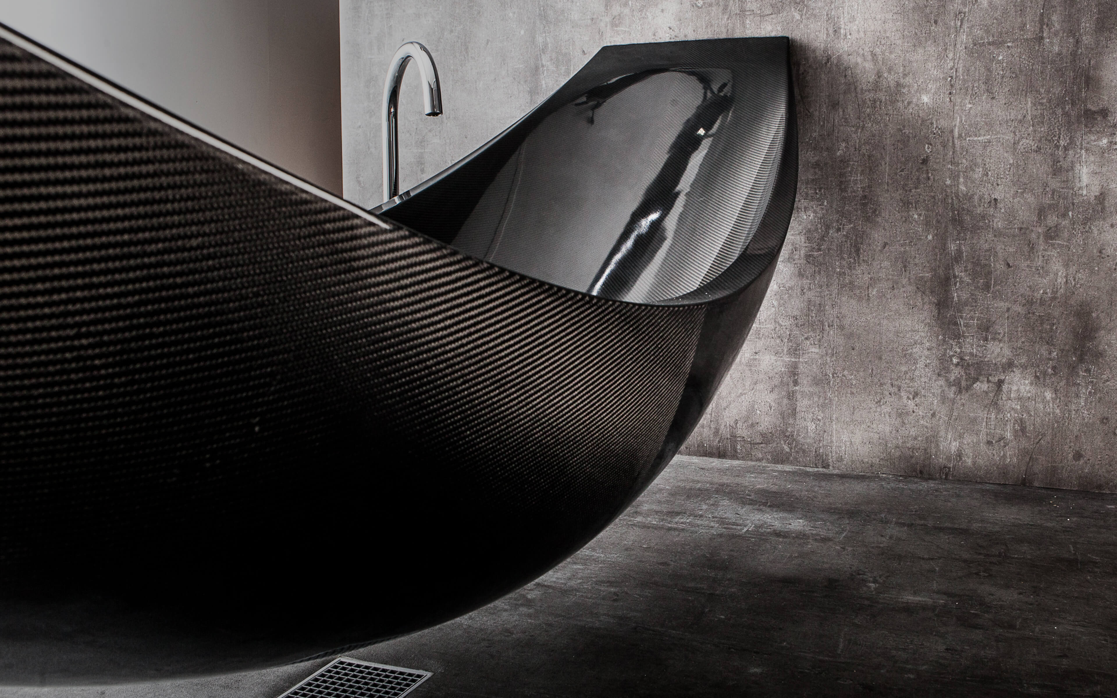 Black carbon fibre hammock bath suspended between concrete wall by Splinterworks