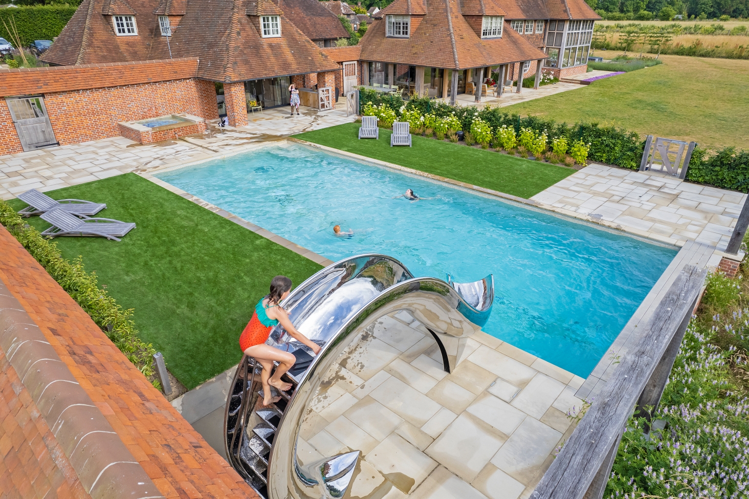 Birds eye view of young girl at the top of a waha pool slide, surronded by English country house and gardens