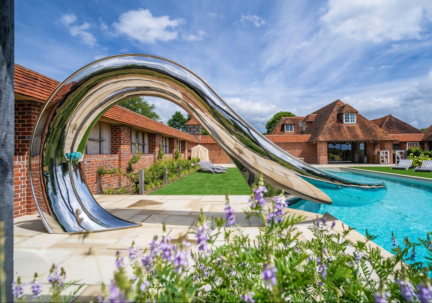 Sculptural, stainless steel pool slide in front of an English country house.