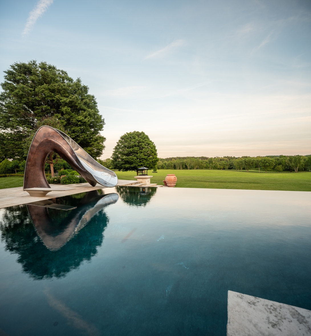 View across swimming pool of bronze vertex, with field and tress behind