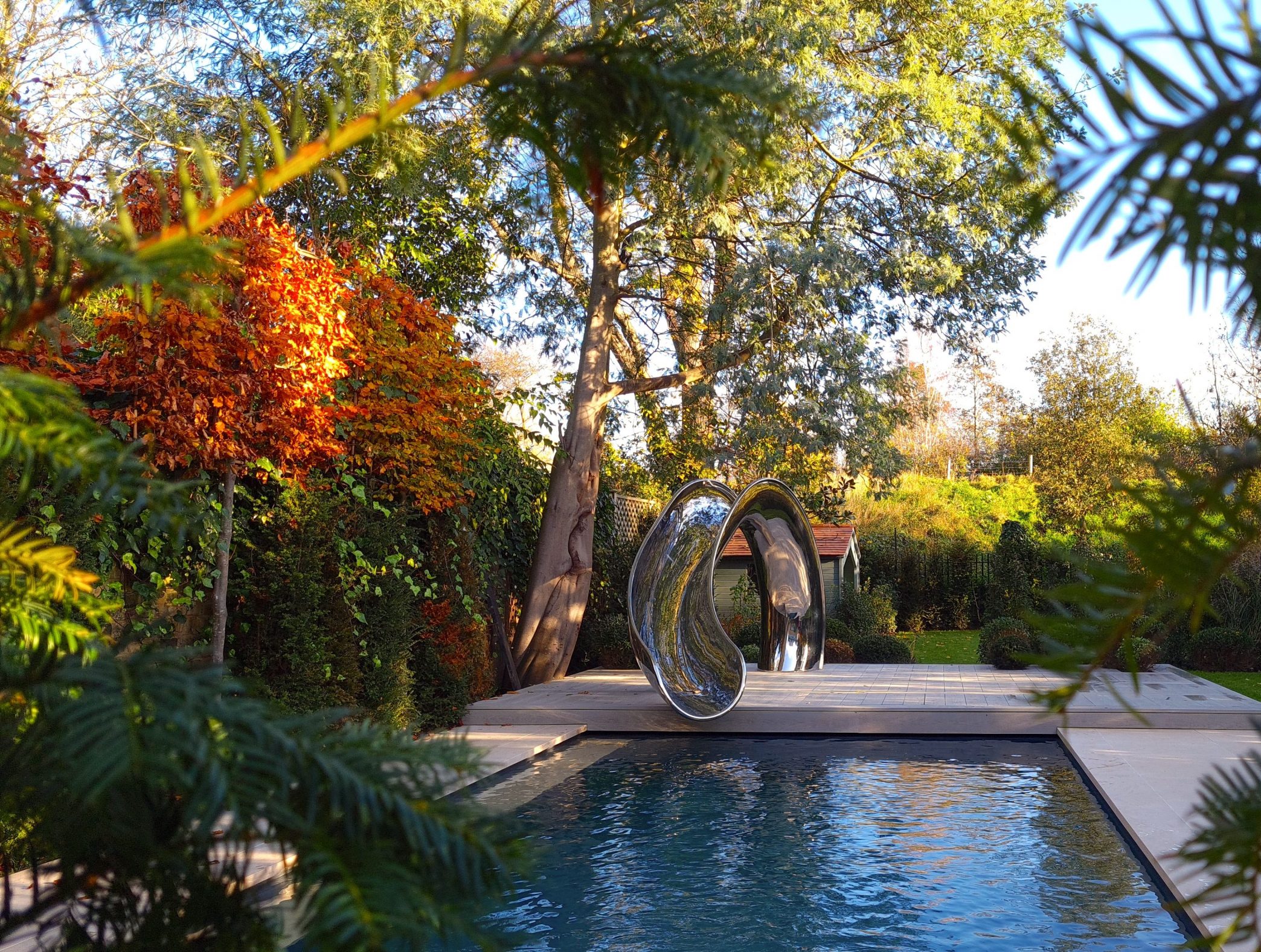 Sculptural stainless steel water slide, surronded by auntumnal trees