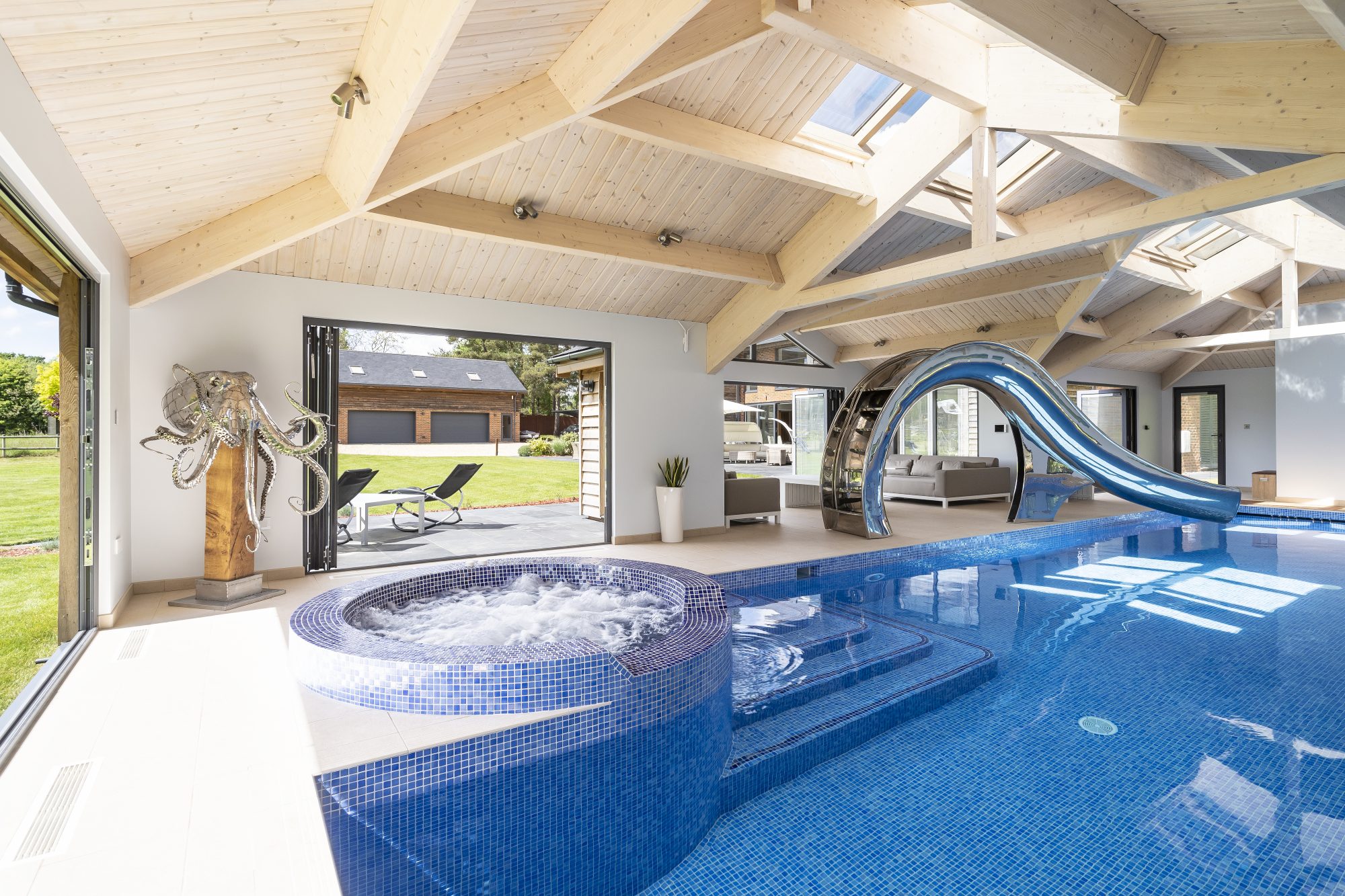 Indoor pool house with curved water slide, Jacuzzi, octopus sculpture and doors to the garden