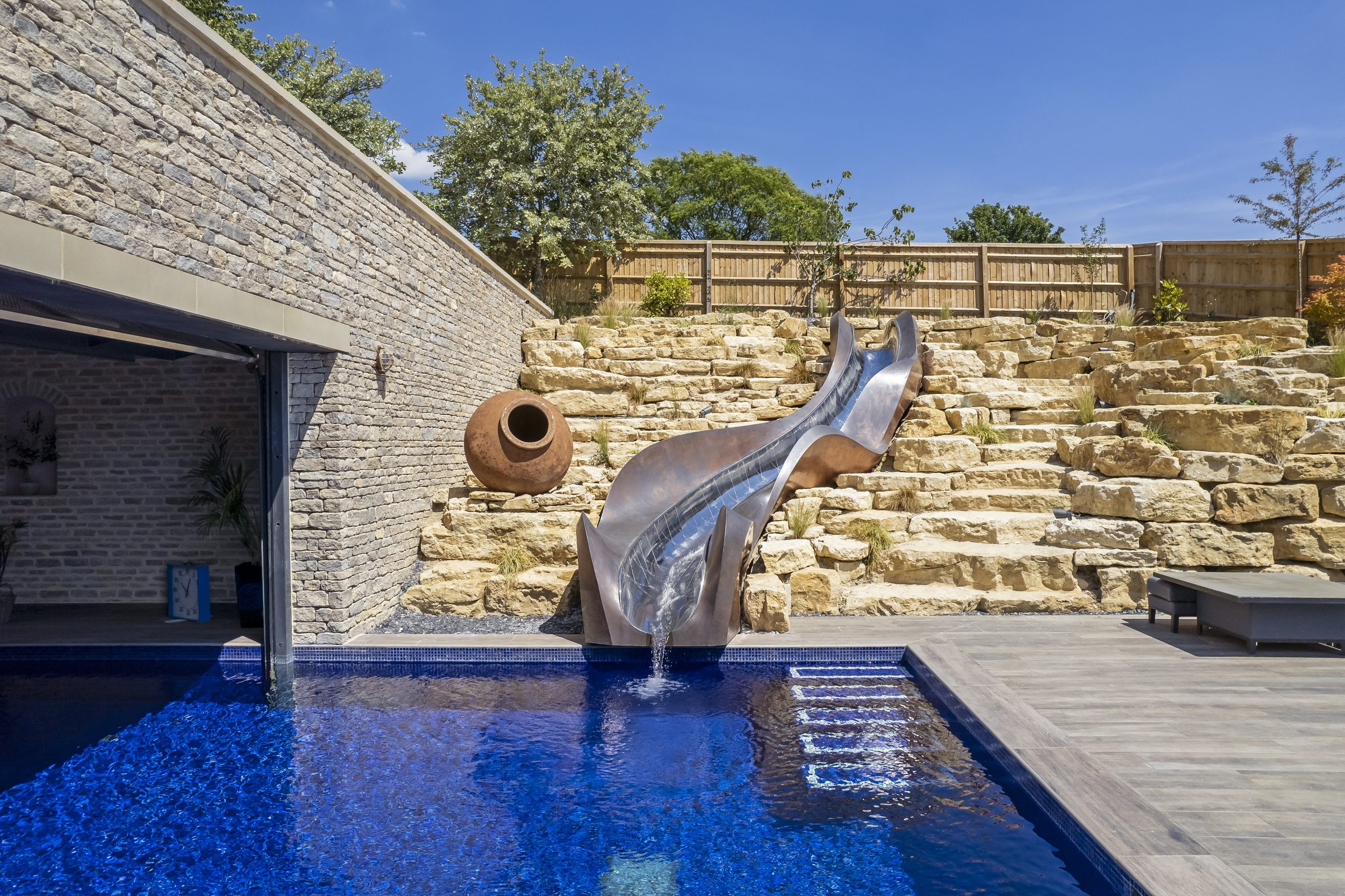 Copper water slide on a backdrop of stepped stones, with indoor/outdoor pool