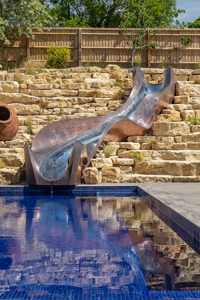 Bronze slide cascading down rockery garden into swimming pool