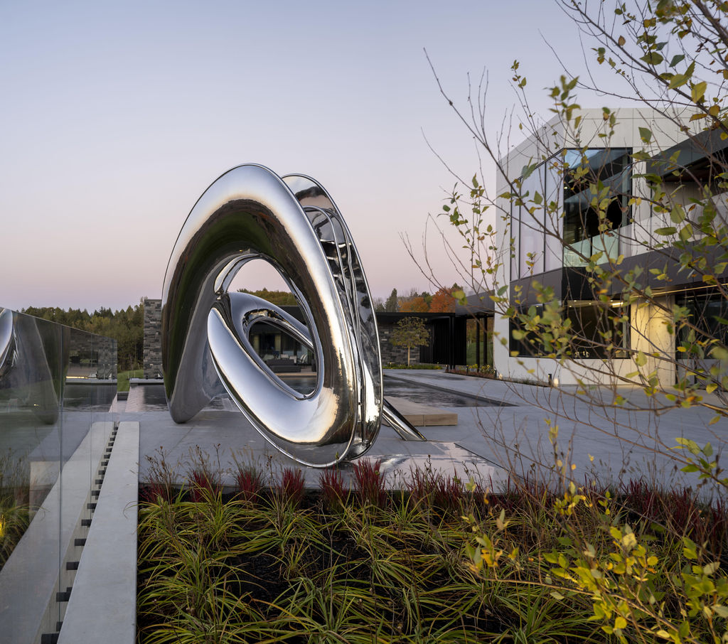 Curved stainless steel back of the Tryst slide, with foliage in the foreground and house in the background.