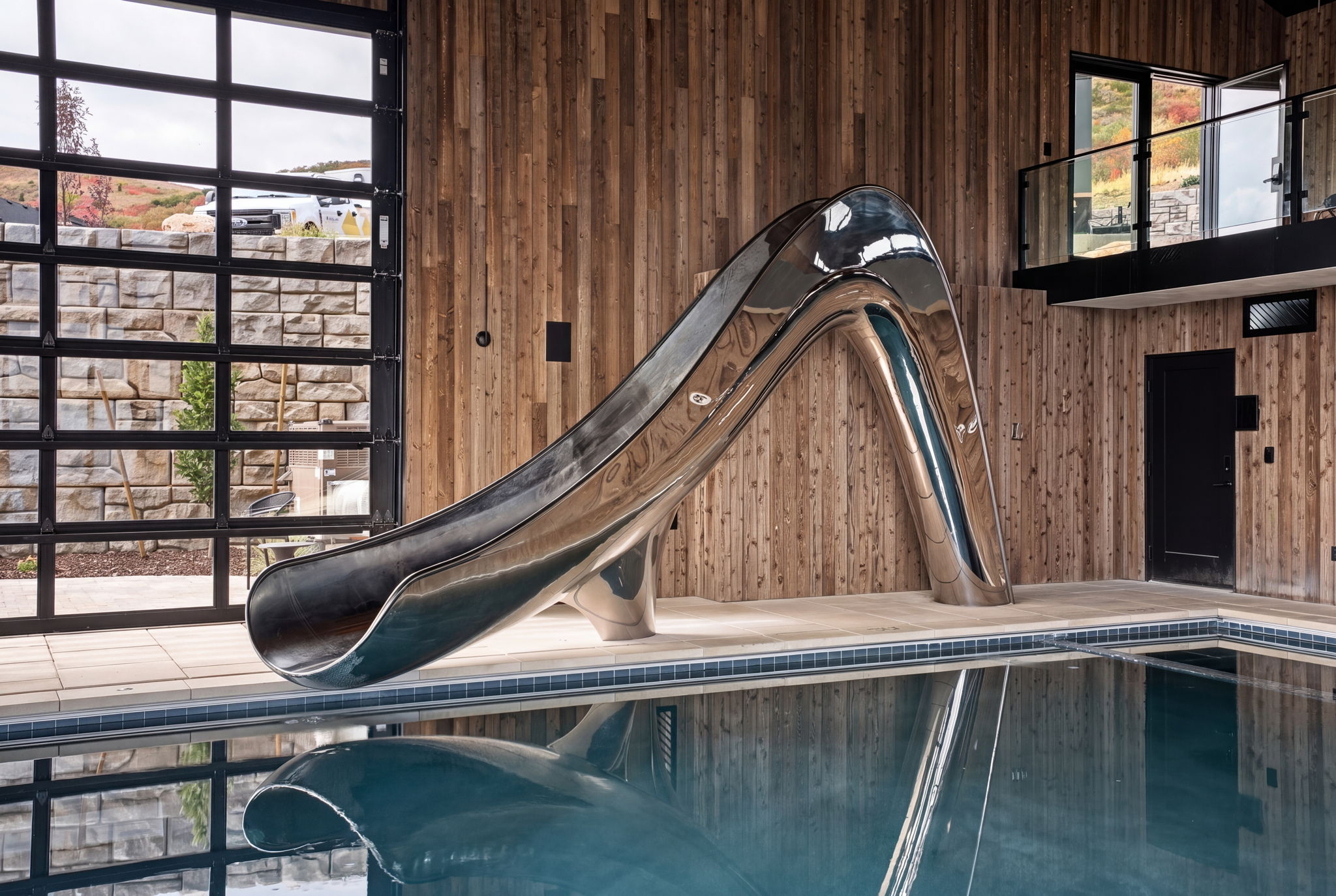 Sleek, space-saving custom metal pool slide sculpture installed along the edge of a luxury indoor pool house.